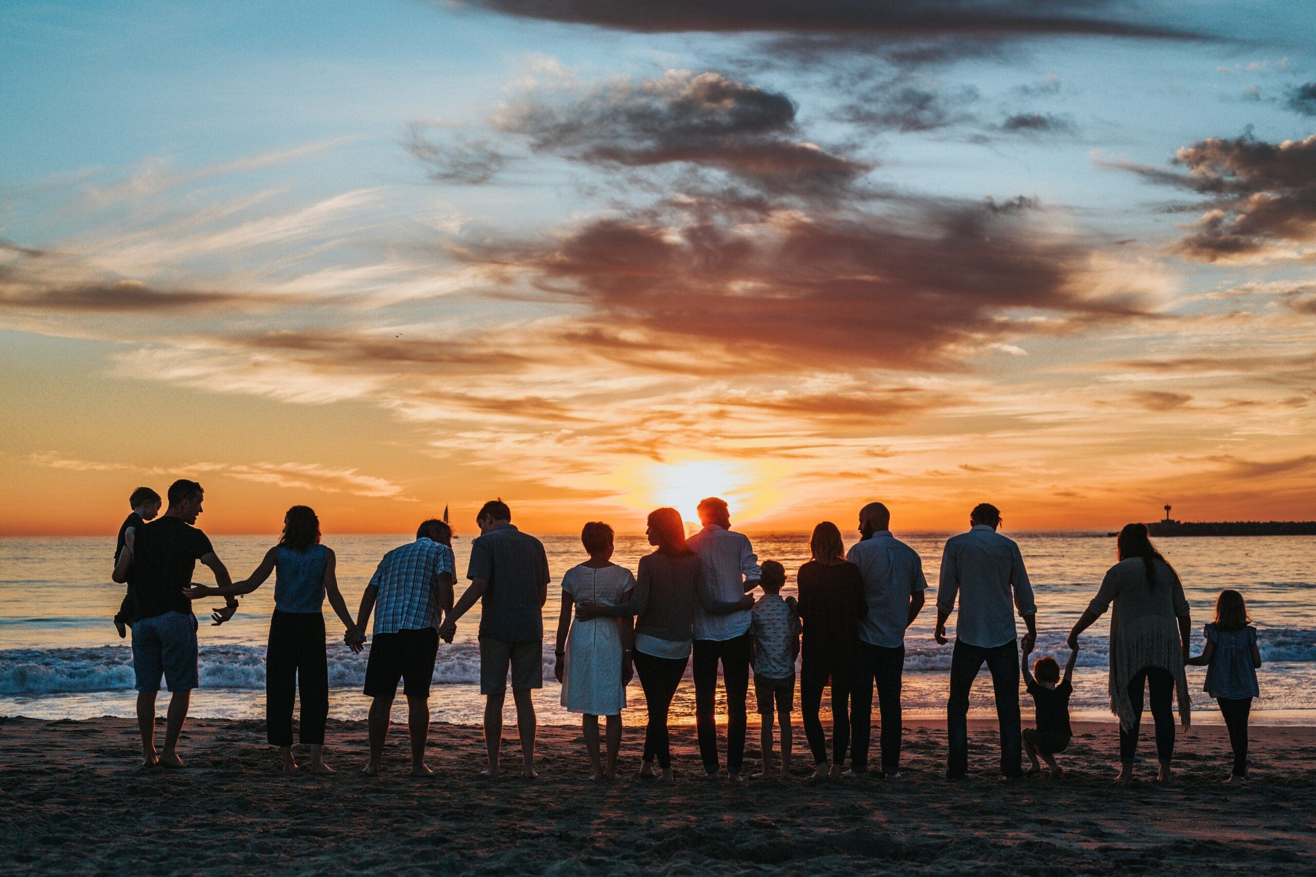 Blended family holding hands on the beach at sunset.
