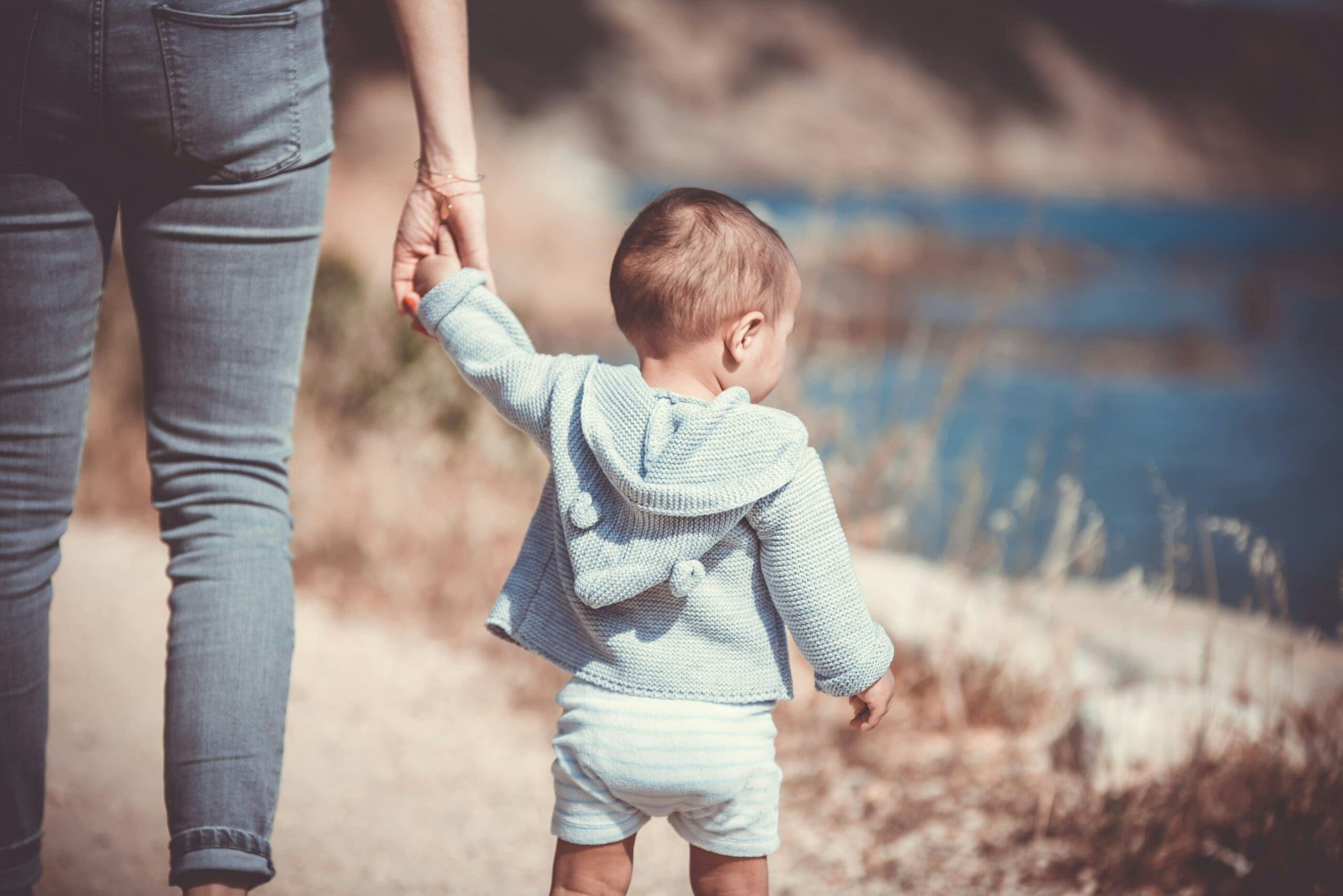 A toddler taking confident steps while holding an adult's hand, capturing the guiding support of the adoption process in Australia.