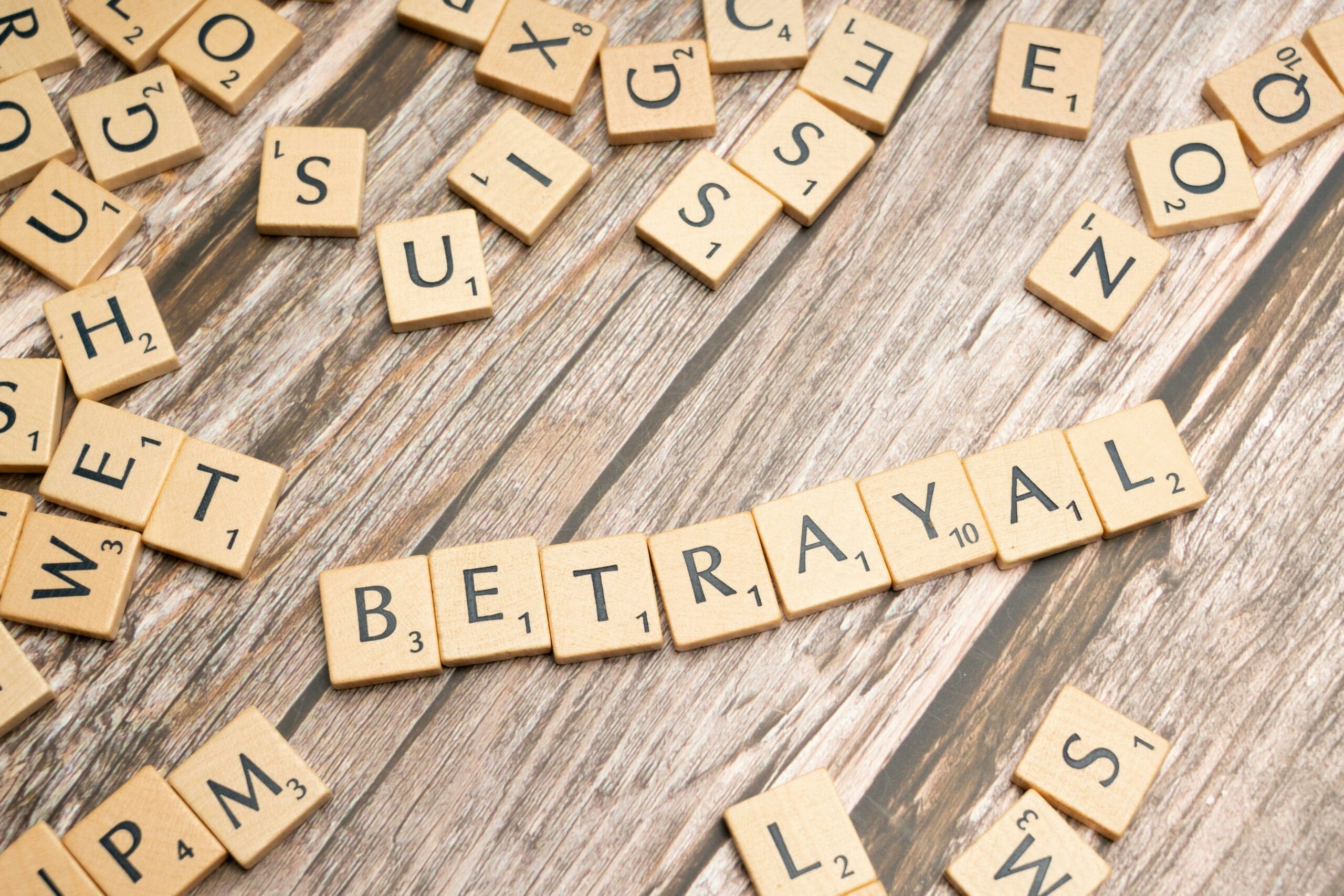 Scrabble tiles spelling out 'BETRAYAL' on a wooden background, symbolising the breach of trust in infidelity and divorce.